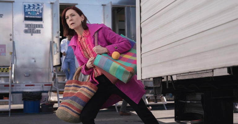 Elsbeth leans out from behind a trailer to do some detective work with multiple tote bags on each arm